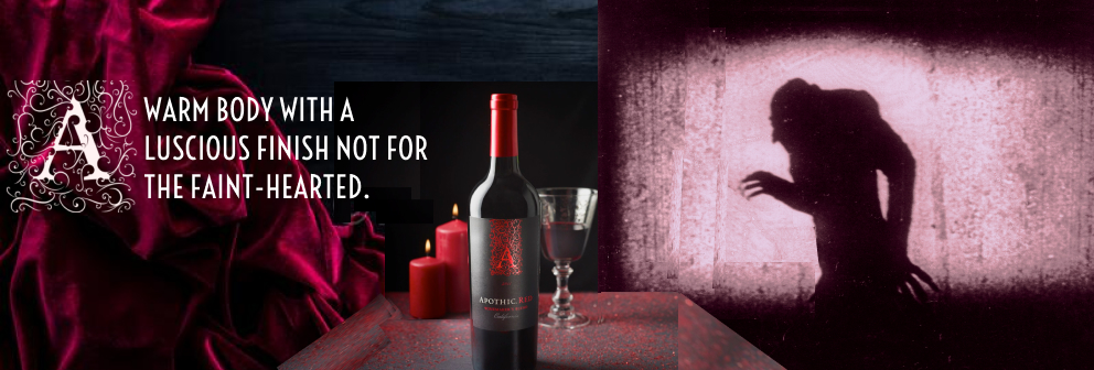 A dark interior space with a table, movie screen and red velvet curtain. A wine bottle, wine glass and candles are on the table. The silhouette of a vampire appears on the movie screen.