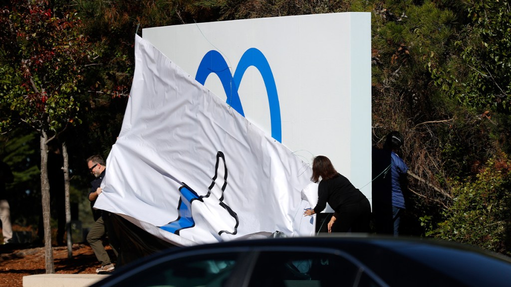 Two people removing a plastic cover from a large outdoor sign to reveal Meta's new brand logo.